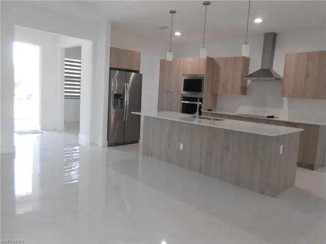 Kitchen featuring decorative light fixtures, stainless steel appliances, modern cabinets, light stone countertops, and a center island with sink