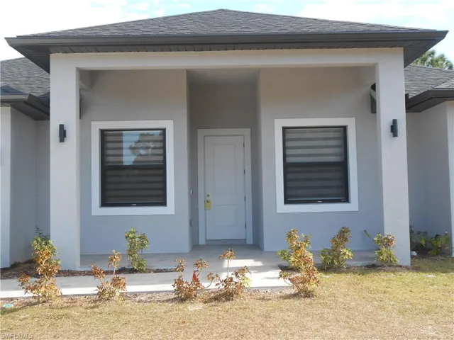 View of exterior entry featuring a shingled roof, stucco siding, a yard, and covered porch