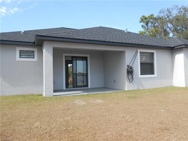 Back of property featuring a lawn, a patio, a shingled roof, and stucco siding