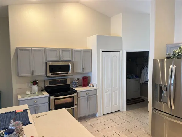 Kitchen with gray cabinetry, light tile patterned flooring, appliances with stainless steel finishes, and washer / clothes dryer