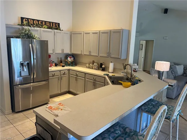 Kitchen with sink, kitchen peninsula, gray cabinets, light tile patterned floors, and stainless steel refrigerator with ice dispenser