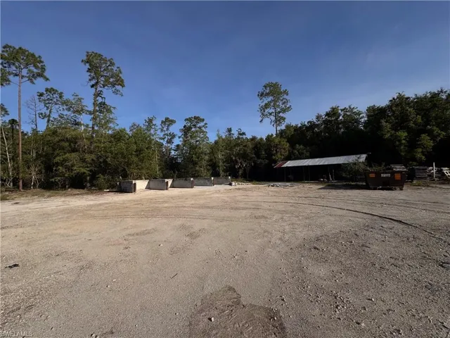 Expansive gravel lot surrounded by mature trees, featuring a large pole barn structure with a corrugated metal roof