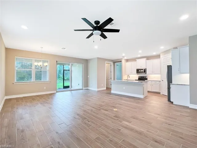 Unfurnished living room with ceiling fan, wood finish floors, and a chandelier