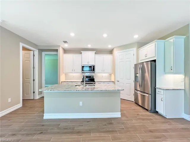 Kitchen featuring light stone counters, stainless steel appliances, white cabinets, wood finish floors, and recessed lighting