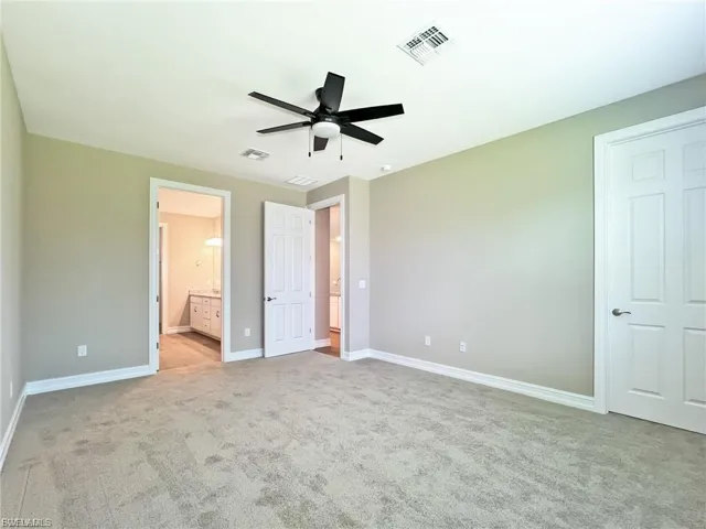 Unfurnished bedroom featuring light carpet, a ceiling fan, and ensuite bath