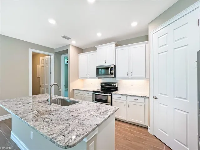Kitchen featuring wood tiled floors, stainless steel appliances, white cabinets, light stone countertops, and an island with sink