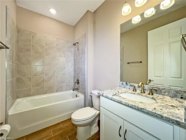 Bathroom featuring washtub / shower combination, vanity, and wood finish floors