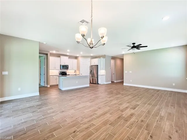 Kitchen featuring open floor plan, a chandelier, white cabinetry, wood finish floors, and stainless steel appliances