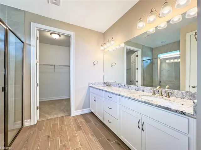 Bathroom with a spacious closet, double vanity, a stall shower, and wood tiled floors