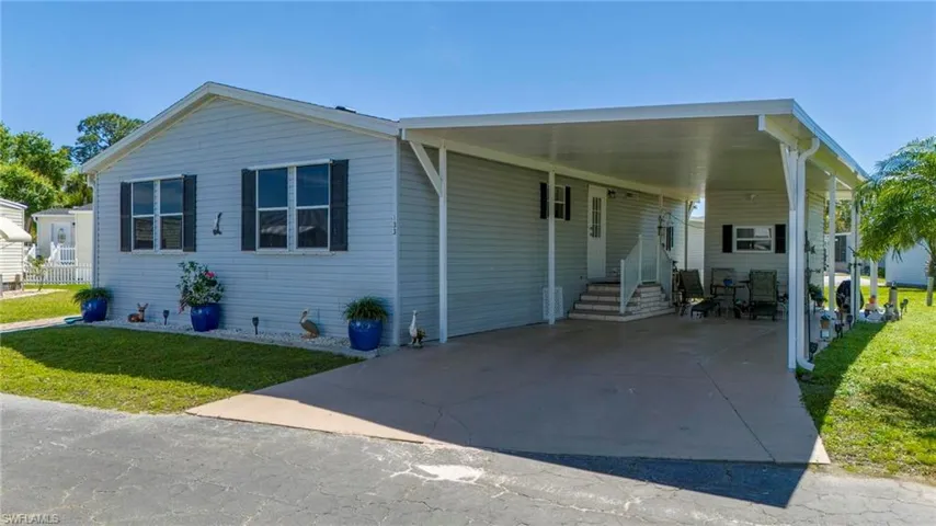 View of front of house featuring an attached carport, a front lawn, driveway, entry steps, and a patio area