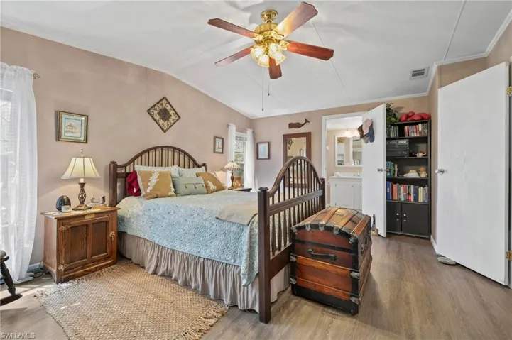 Bedroom with wood finished floors, vaulted ceiling, crown molding, a ceiling fan, and connected bathroom