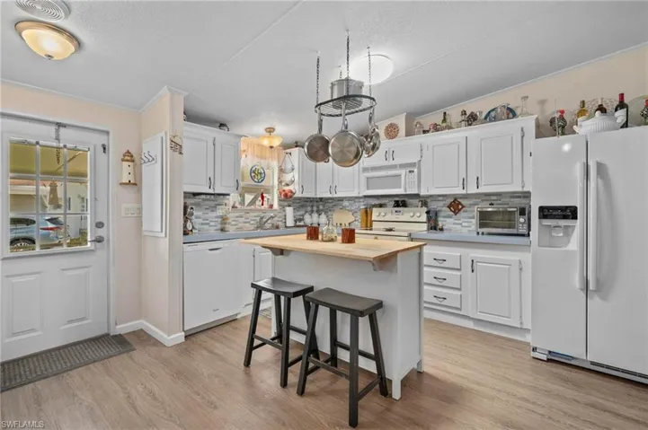 Kitchen featuring white appliances, white cabinetry, a breakfast bar area, crown molding, and a center island