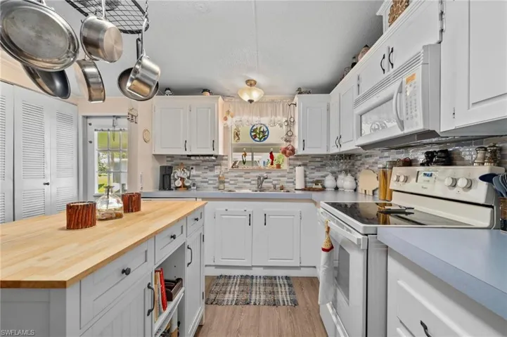 Kitchen with butcher block counters, white appliances, tasteful backsplash, and white cabinetry