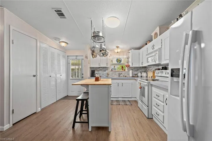 Kitchen featuring white appliances, butcher block counters, a kitchen breakfast bar, decorative backsplash, and light wood-style floors
