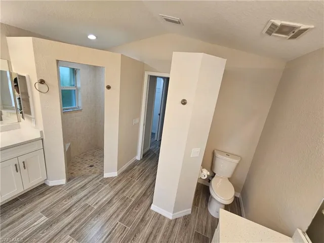 Bathroom with a textured ceiling, lofted ceiling, tiled shower, toilet, and vanity