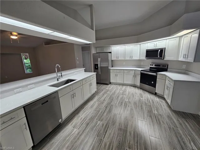 Kitchen featuring light hardwood / wood-style flooring, white cabinetry, vaulted ceiling, stainless steel appliances, and sink