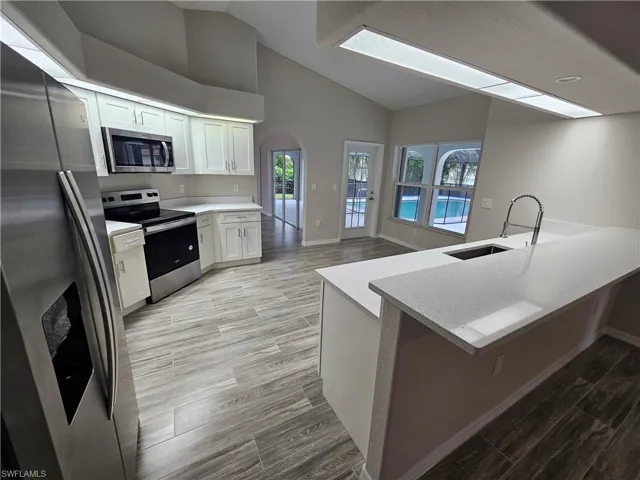 Kitchen featuring stainless steel appliances, light hardwood / wood-style floors, white cabinetry, light stone counters, and sink