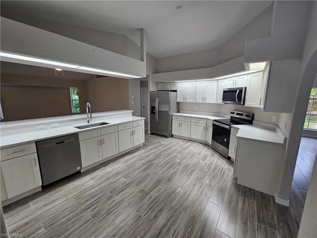 Kitchen featuring appliances with stainless steel finishes, white cabinets, high vaulted ceiling, sink, and light hardwood / wood-style flooring