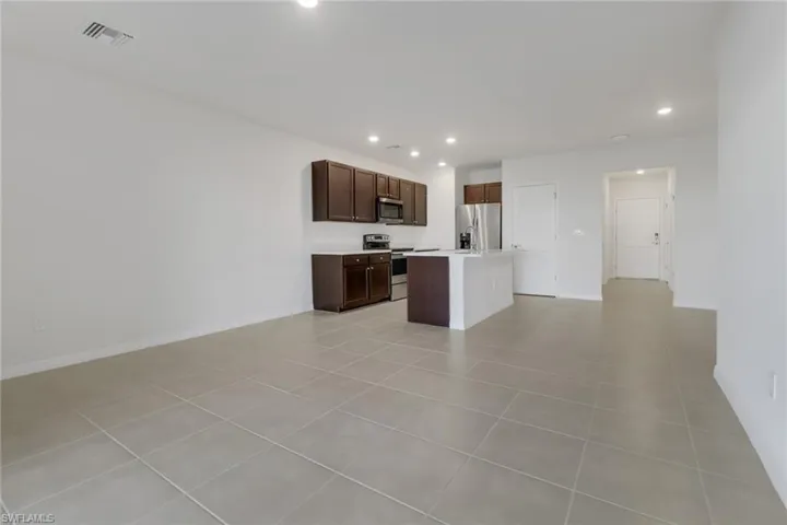 Kitchen featuring dark brown cabinetry, stainless steel appliances, a kitchen island, and light tile patterned flooring