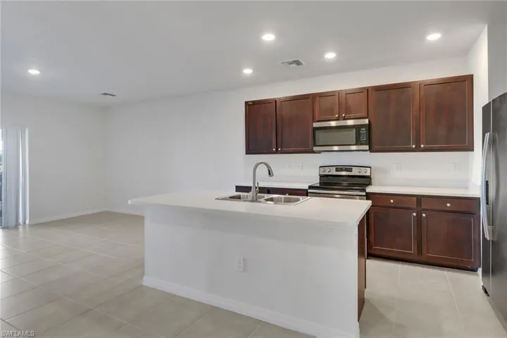 Kitchen featuring sink, light tile patterned floors, stainless steel appliances, and an island with sink