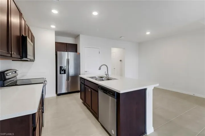 Kitchen featuring a center island with sink, sink, light tile patterned floors, appliances with stainless steel finishes, and dark brown cabinetry