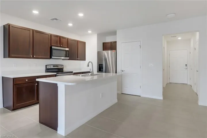 Kitchen with dark brown cabinetry, sink, stainless steel appliances, an island with sink, and light tile patterned floors