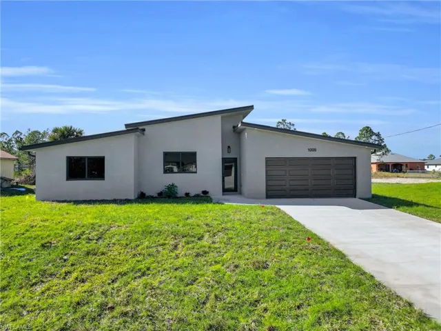 Mid-century modern home featuring a front lawn, stucco siding, concrete driveway, and a garage