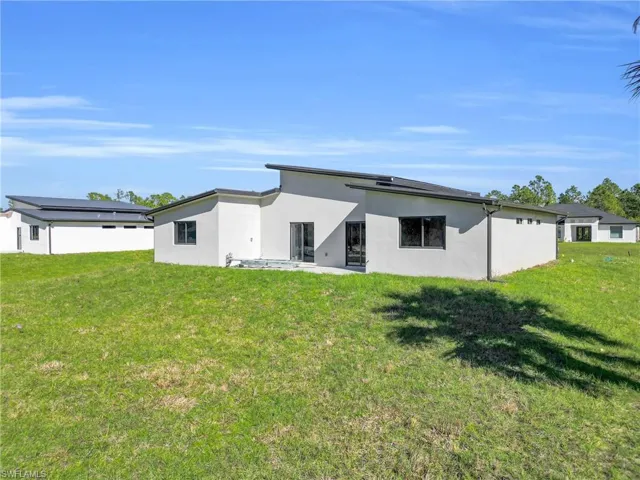 Back of house with stucco siding, a lawn, and a patio area