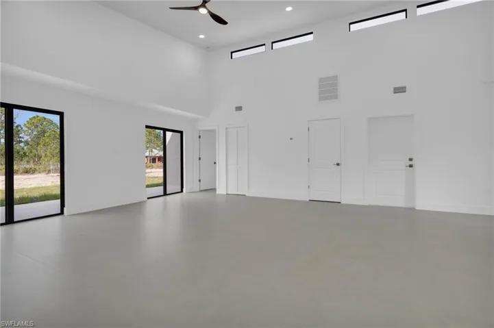 Empty room featuring ceiling fan, concrete flooring, recessed lighting, and a towering ceiling