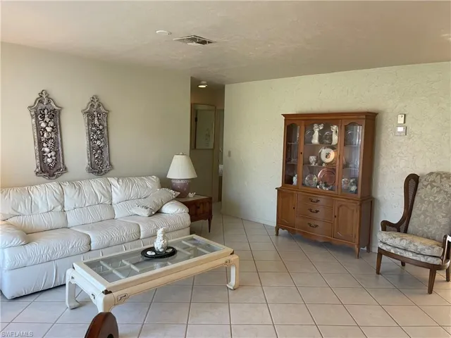 Living room featuring visible vents, a textured wall, and light tile patterned floors