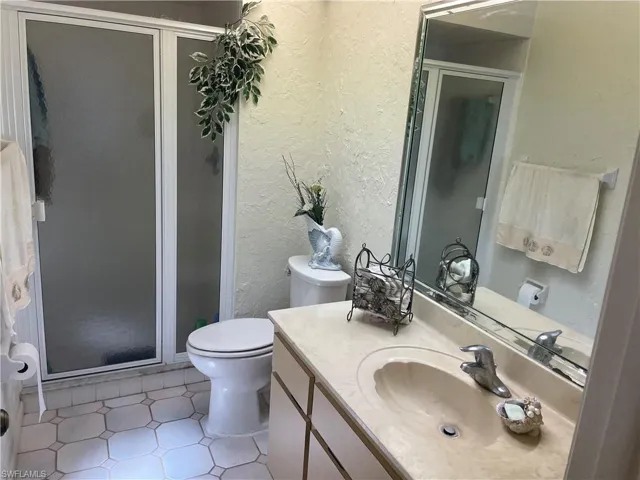 Full bath with toilet, a shower stall, vanity, and a textured wall