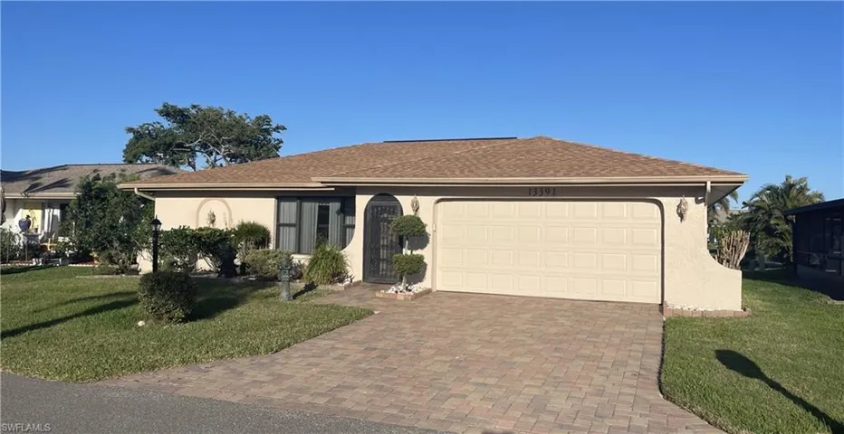 Ranch-style house featuring a garage, a shingled roof, stucco siding, decorative driveway, and a front yard