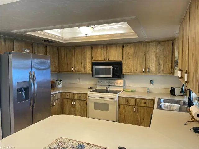 Kitchen featuring black microwave, a sink, stainless steel fridge with ice dispenser, a tray ceiling, and white electric range oven