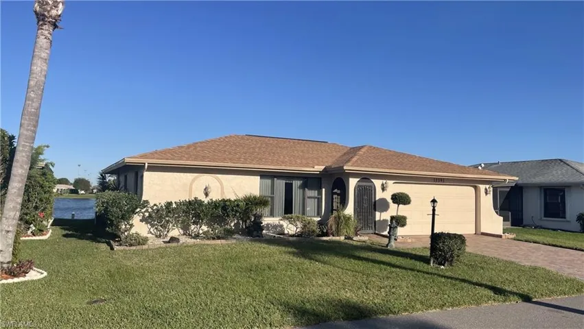 Ranch-style home with decorative driveway, stucco siding, a shingled roof, an attached garage, and a front yard