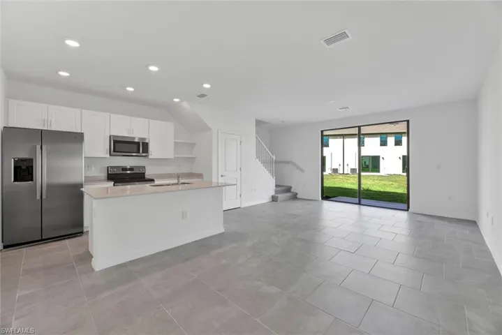 Kitchen featuring stainless steel appliances, white cabinets, a kitchen island with sink, open floor plan, and recessed lighting