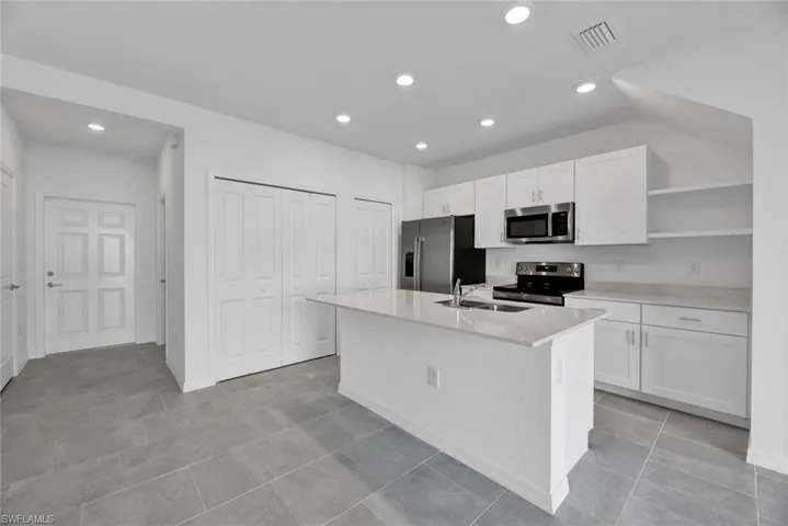 Kitchen featuring white cabinets, open shelves, appliances with stainless steel finishes, recessed lighting, and a center island with sink