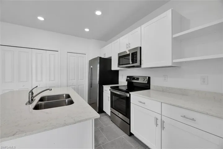 Kitchen featuring open shelves, stainless steel appliances, light stone counters, white cabinetry, and recessed lighting