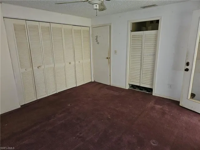 Unfurnished bedroom featuring dark colored carpet, ceiling fan, and a textured ceiling