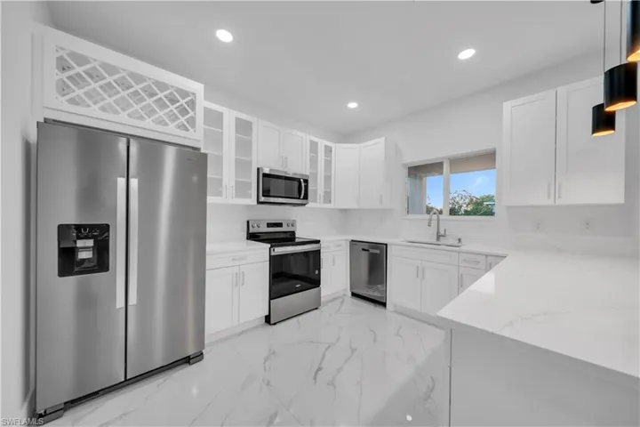 Kitchen featuring stainless steel appliances, recessed lighting, light stone countertops, white cabinetry, and light marble finish flooring