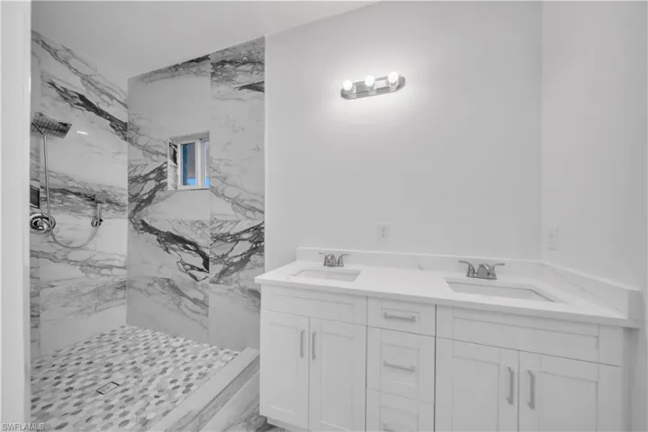 Full bath with double vanity and a marble finish shower