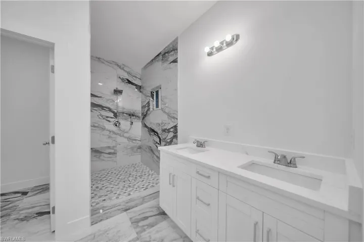 Bathroom with light marble finish flooring, double vanity, and a marble finish shower