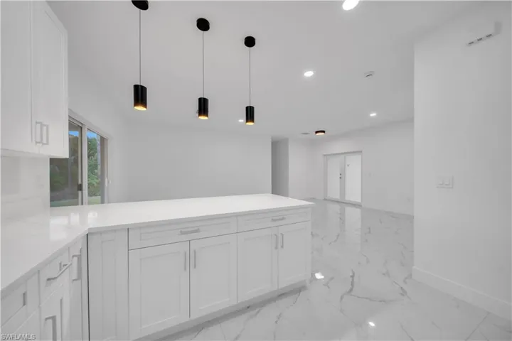 Kitchen featuring white cabinets, light stone counters, decorative light fixtures, a peninsula, and open floor plan