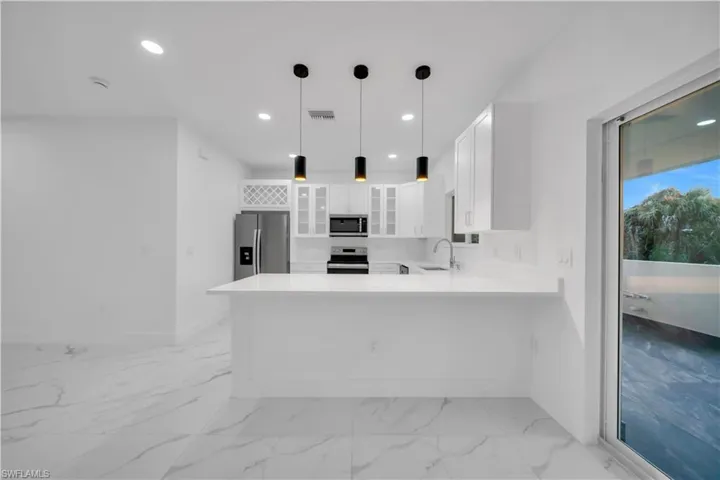 Kitchen featuring glass fronted cabinets, white cabinets, a peninsula, stainless steel appliances, and hanging light fixtures