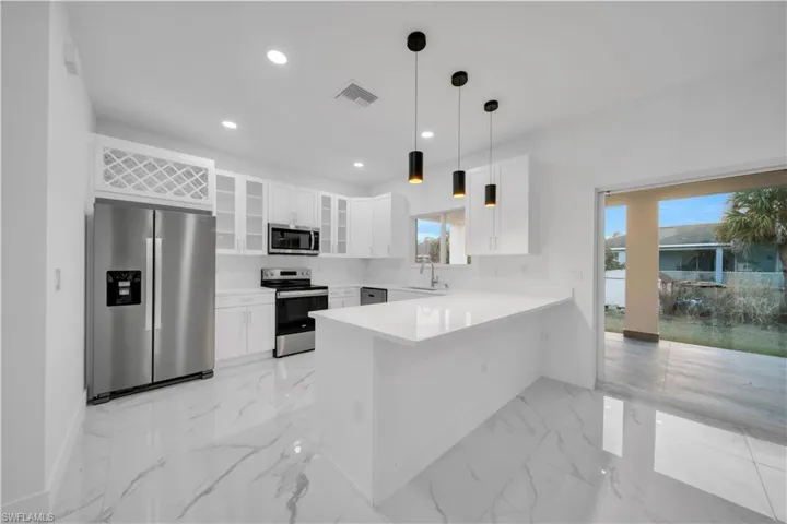 Kitchen with stainless steel appliances, white cabinets, a peninsula, glass insert cabinets, and decorative light fixtures