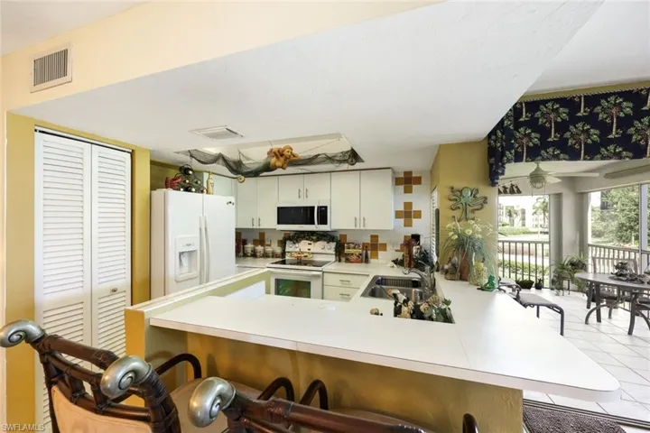Kitchen featuring white appliances, a breakfast bar area, visible vents, a peninsula, and a sink
