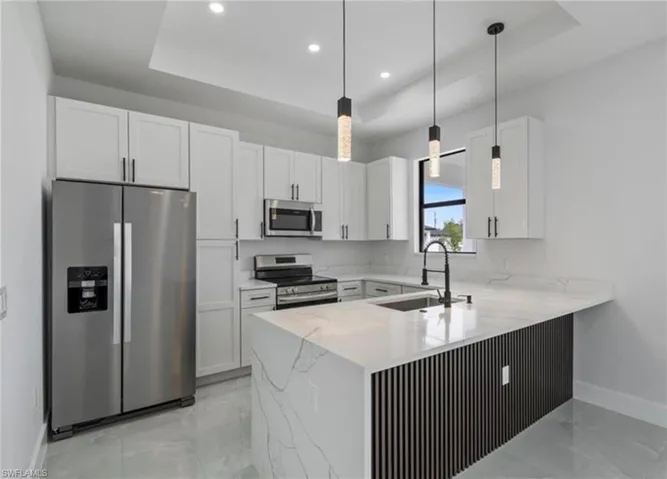 Kitchen featuring stainless steel appliances, white cabinetry, a raised ceiling, light stone counters, and hanging light fixtures