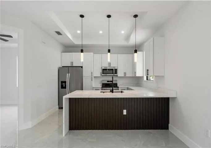 Kitchen featuring a peninsula, white cabinetry, stainless steel appliances, a raised ceiling, and hanging light fixtures