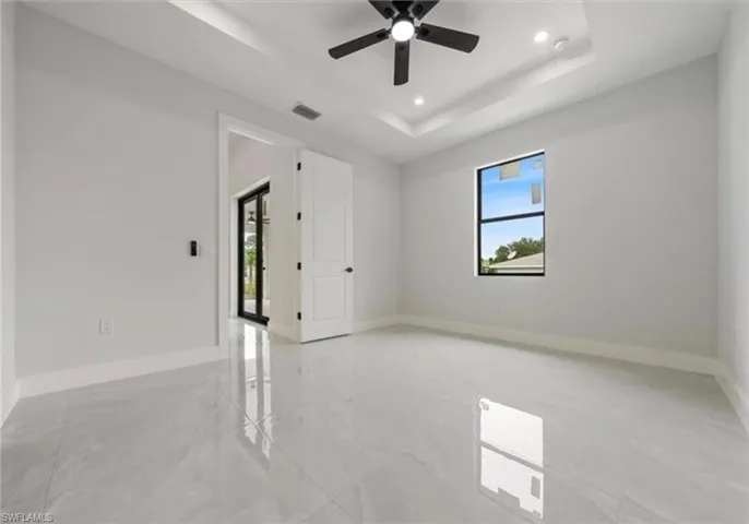 Spare room featuring healthy amount of natural light, a raised ceiling, recessed lighting, light marble finish flooring, and ceiling fan