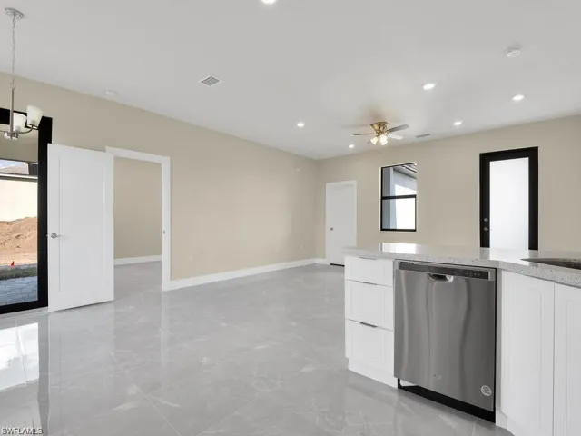 Kitchen featuring light stone counters, white cabinetry, stainless steel dishwasher, a ceiling fan, and a chandelier