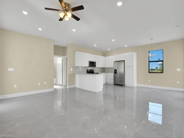 Kitchen featuring open floor plan, white cabinets, stainless steel appliances, decorative light fixtures, and a ceiling fan